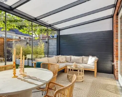 Warme tuinkamer gevuld met houten meubels en met glazen dak