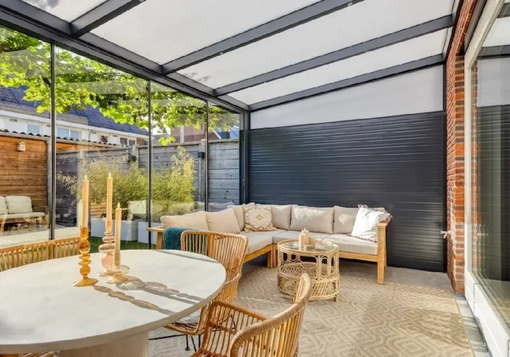 Warme tuinkamer gevuld met houten meubels en met glazen dak